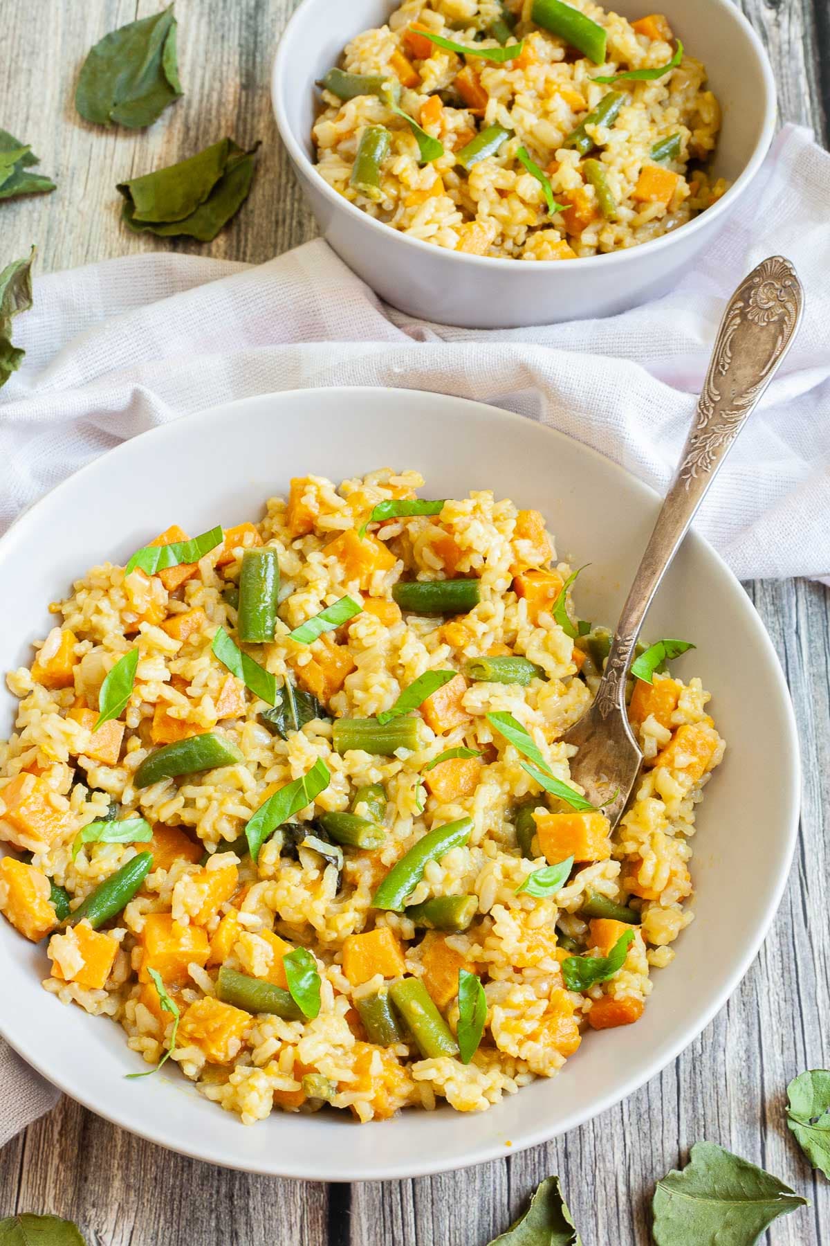 Two white bowls of fried rice in an orange sauce with sweet potato cubes and green bean pieces, A fork is placed inside the dish.