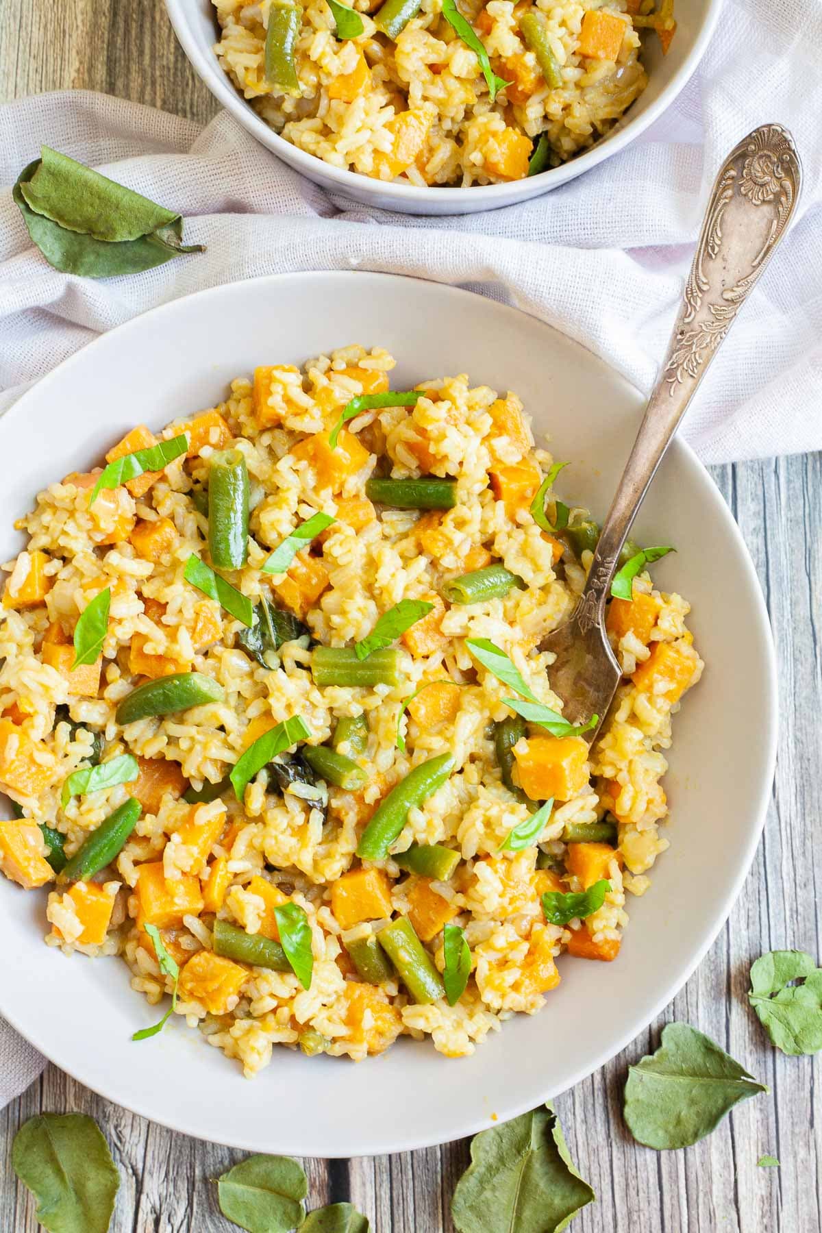 Two white bowls of fried rice in an orange sauce with sweet potato cubes and green bean pieces, A fork is placed inside the dish. 