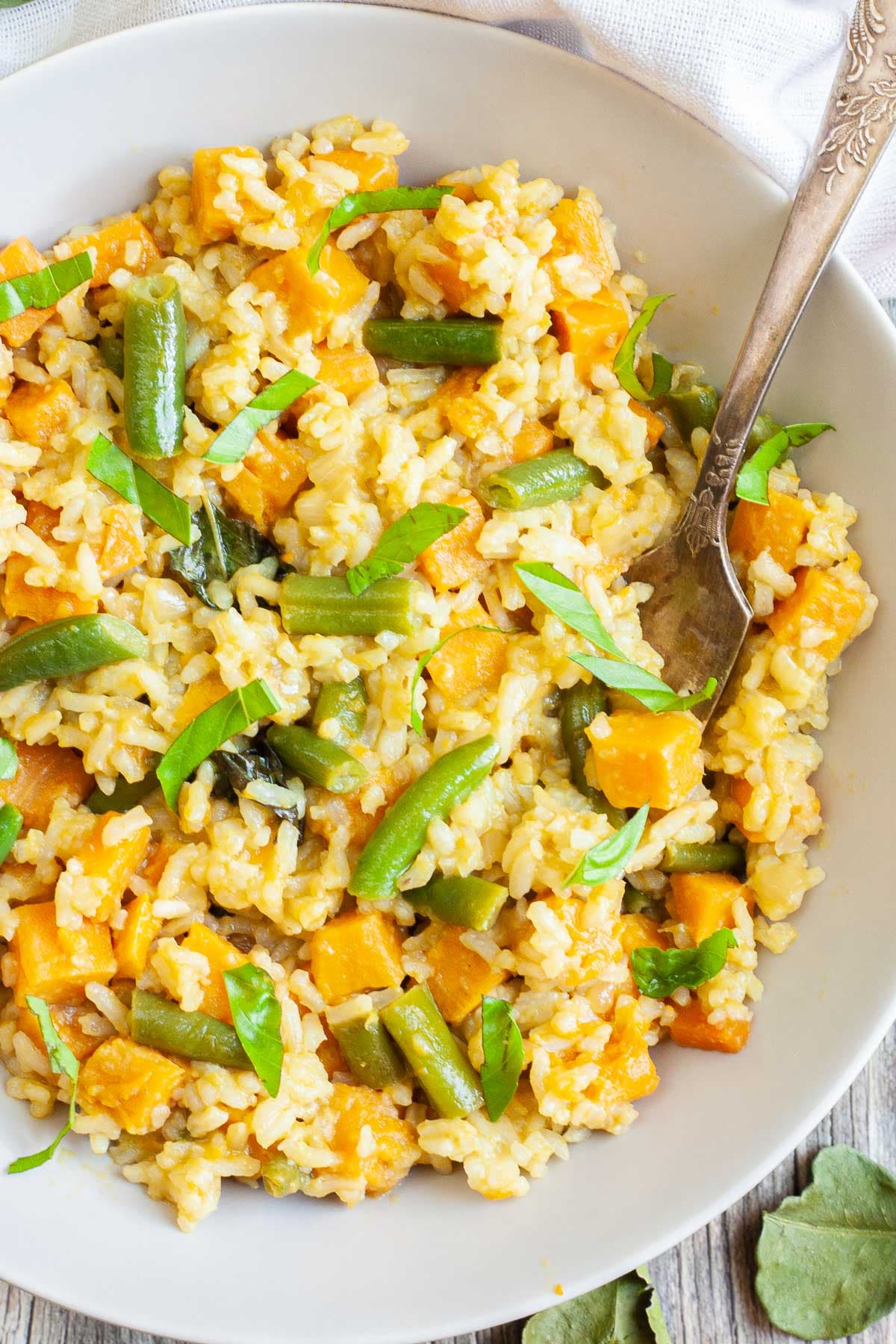 A white bowl of fried rice in an orange sauce with sweet potato cubes and green bean pieces, A fork is placed inside the dish.