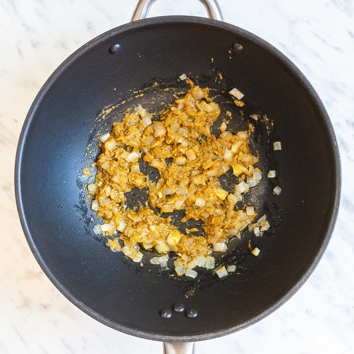 Wok with finely chopped onion in a greenish-brown paste.