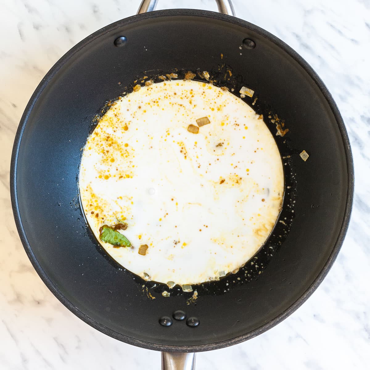 A wok with white liquid and chunks of spice and onion is swimming around. 