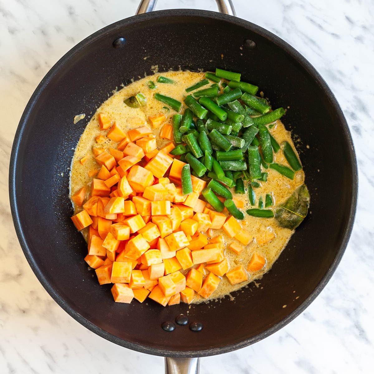 Wok with an orange sauce topped with swet potato cubes and green bean pieces. 