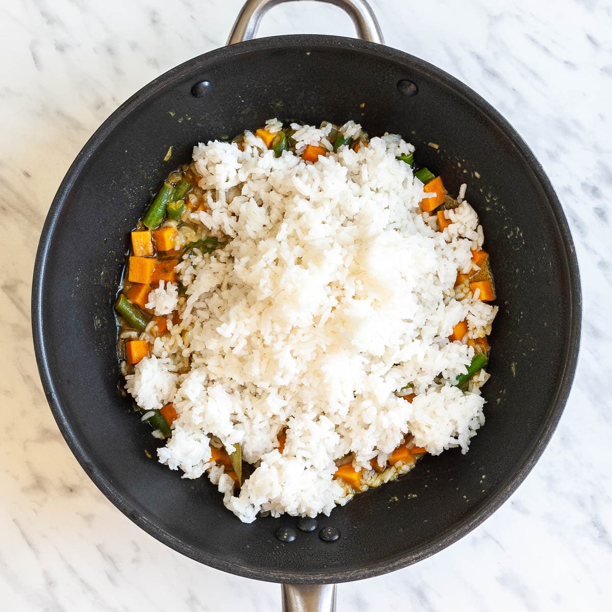 Wok with sweet potato cubes and green bean pieces in an orange sauce topped with a large amount of white rice. 