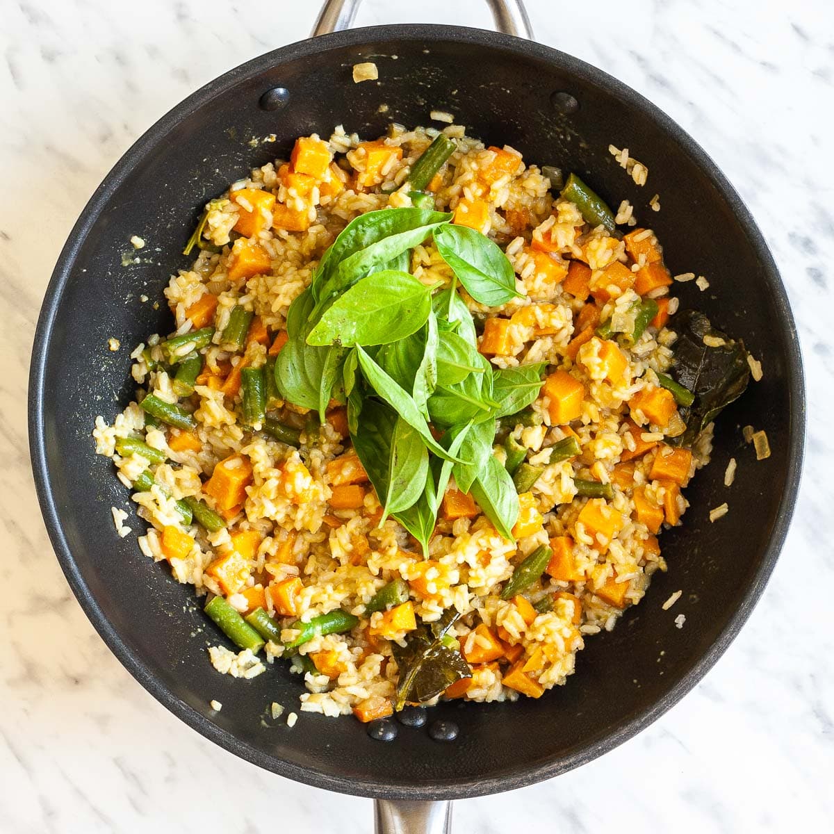 Rice, sweet potato cubes, green bean pieces are stir-fried in an orange sauce topped with some fresh basil leaves