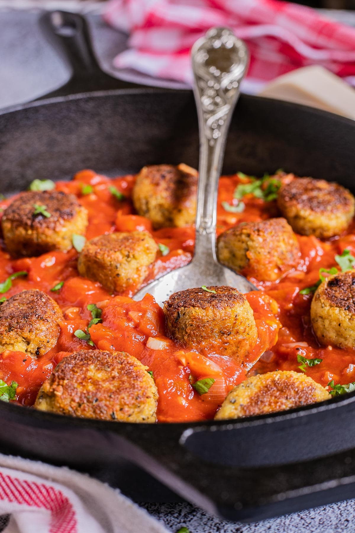 Black cast iron skillet with red marinara sauce and crispy brown tofu meatballs. A large spoon is in the middle.
