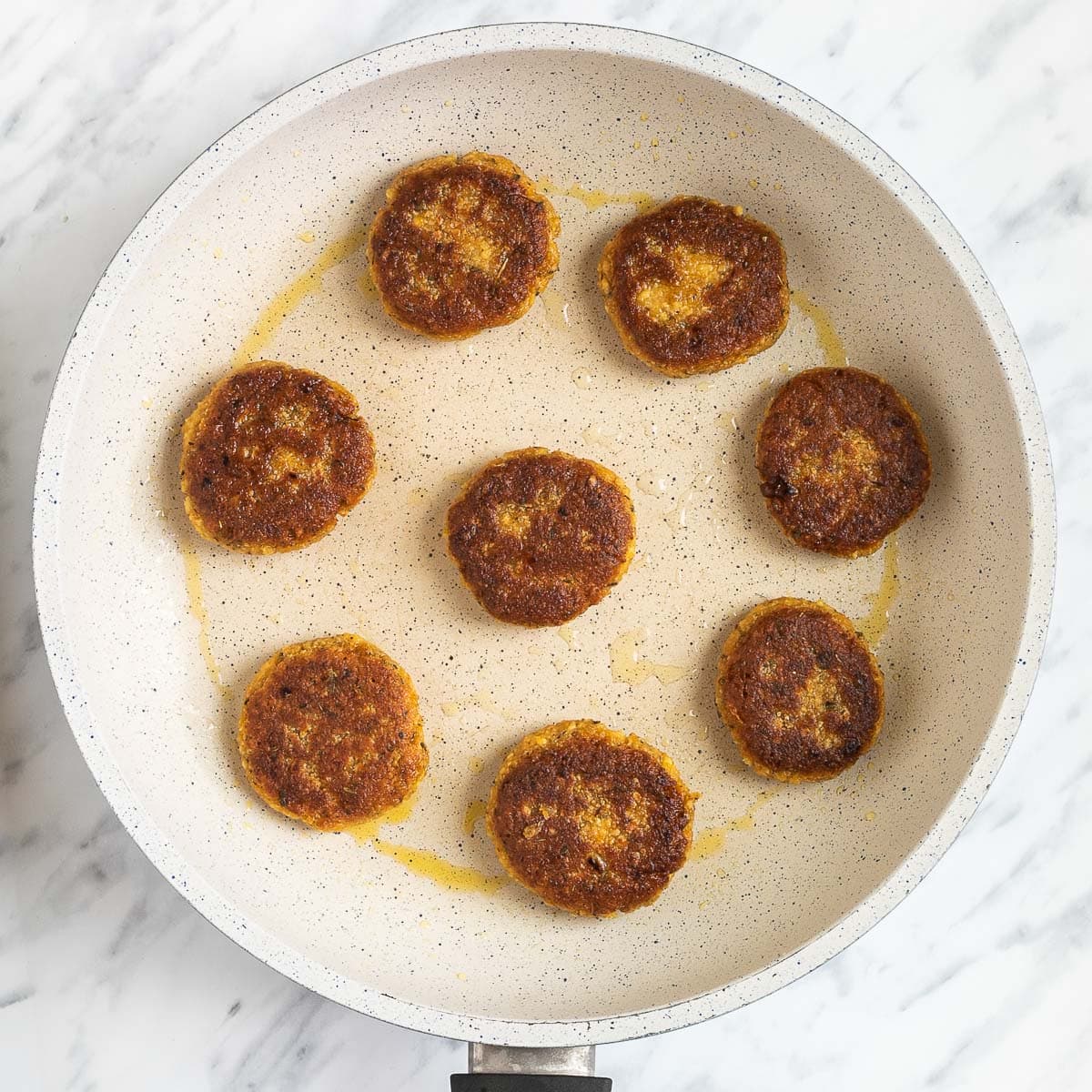 A white frying pan with crispy brown round sausage patties.