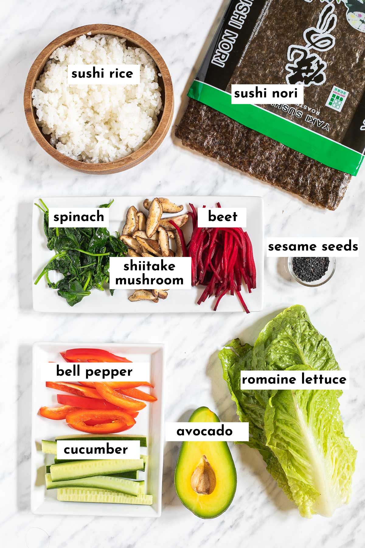 The ingredients of sushi without fish is placed on small white plates like spinach, mushroom, beet slices, cucumber, red pepper strips, half avocado, lettuce leaves, small bowl of rice and nori sheets.  