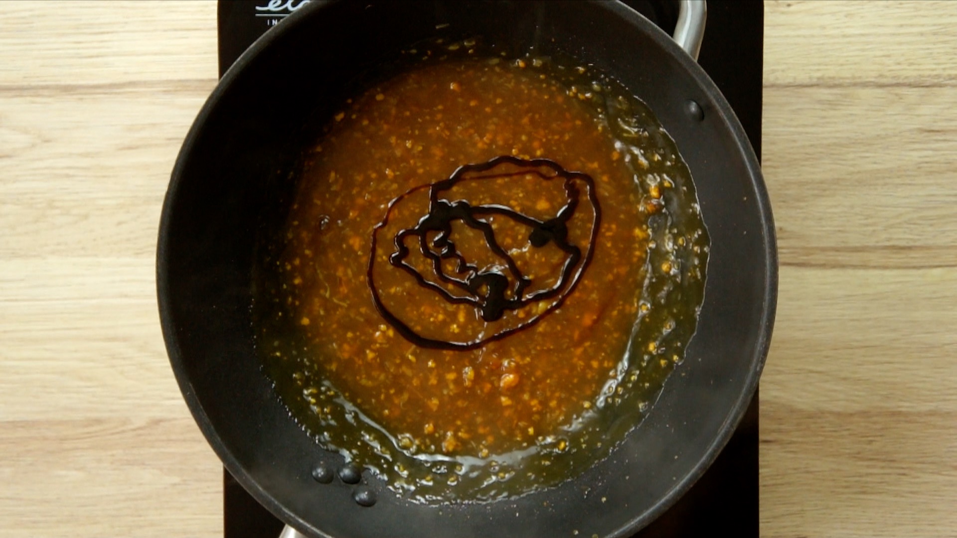 Dark brown sauce with ginger and garlic pieces and a drizzle of black paste in a wok.