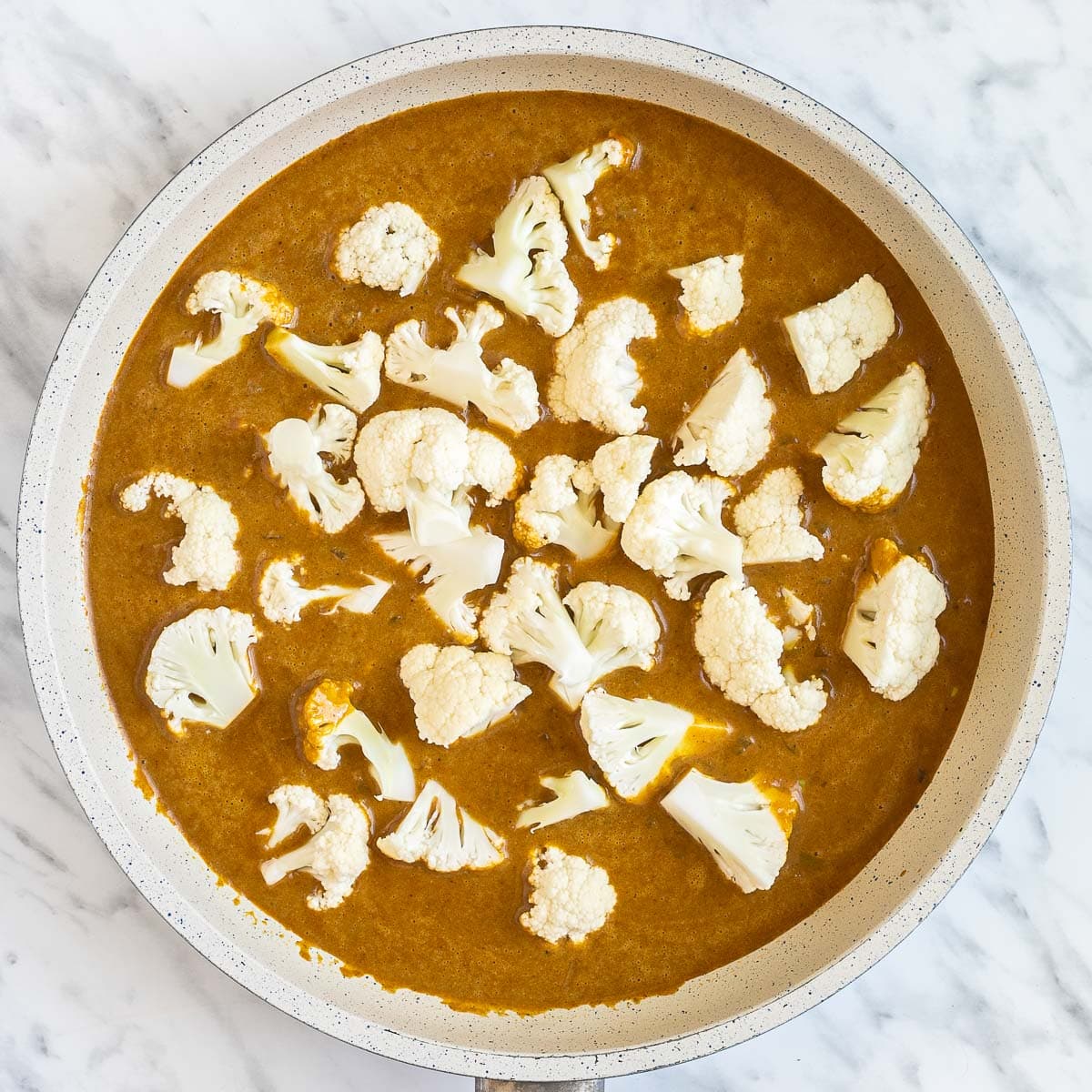 White frying pan with a creamy orange sauce mixed with cauliflower florets.