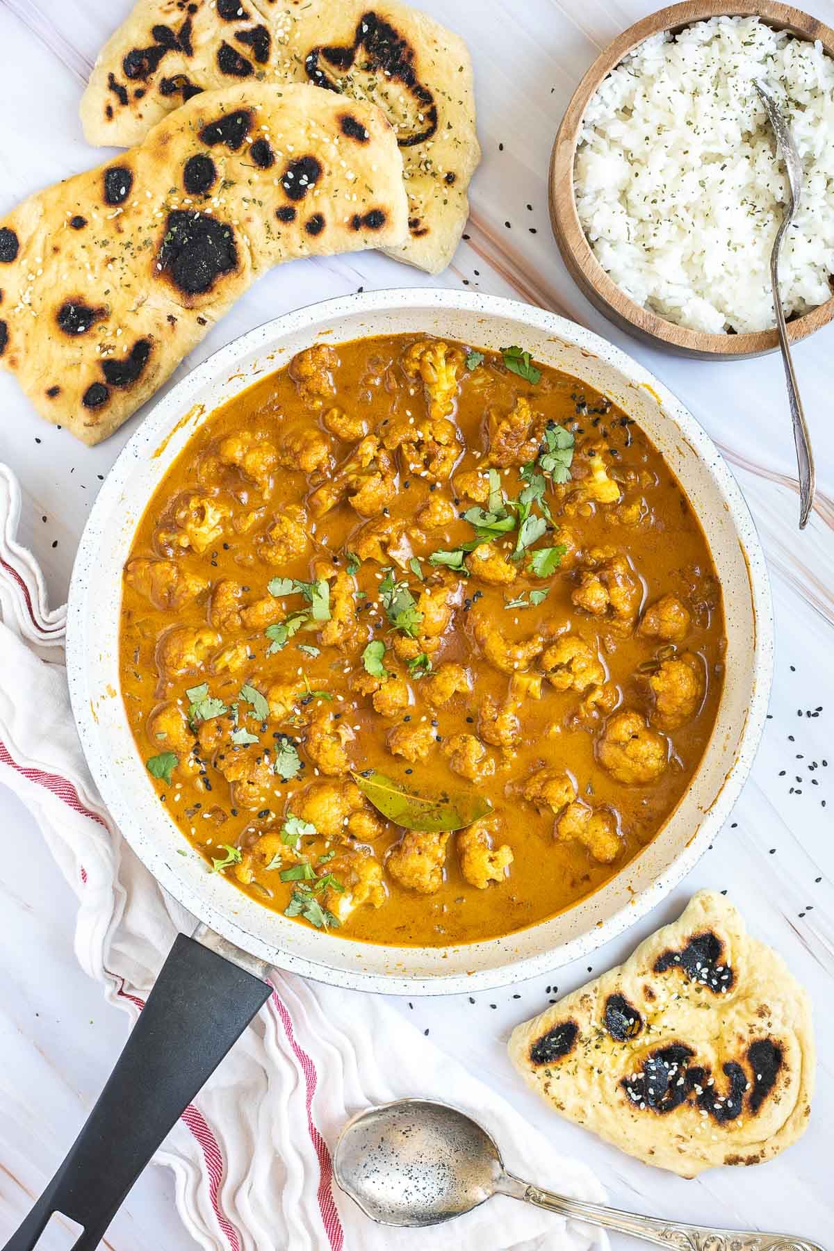 White frying pan with a creamy orange sauce mixed with cauliflower florets, sprinkled with sesame seeds and freshly chopped cilantro.