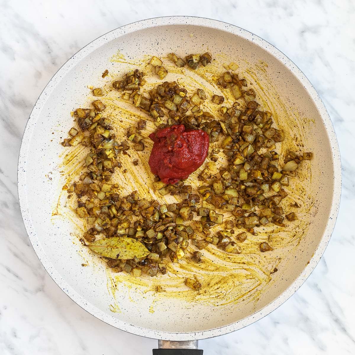 White frying pan with brown chopped onion since the spices previously added colored them with a small dollop of tomato paste.