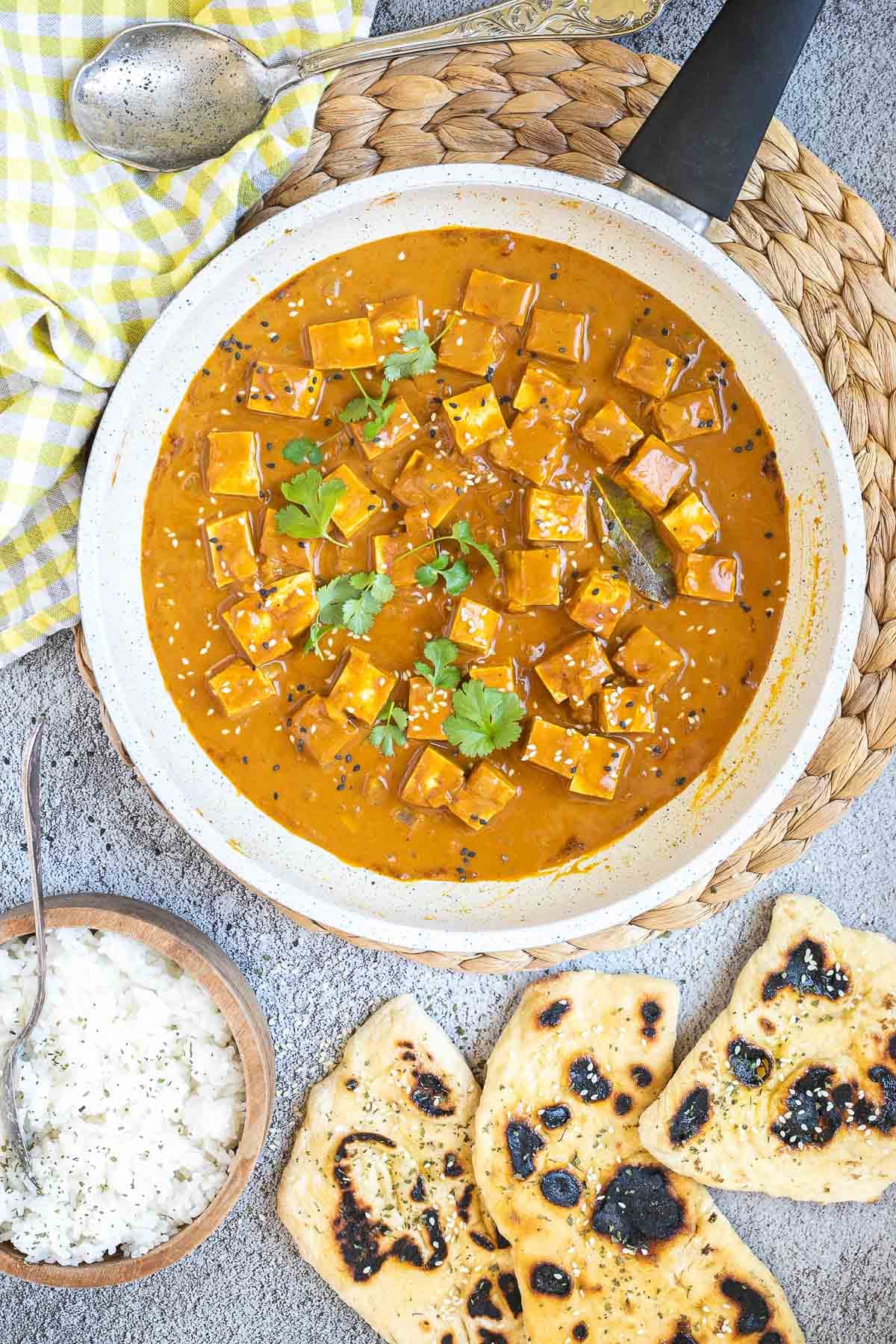 White frying pan with a creamy orange sauce mixed with tofu cubes, sprinkled with sesame seeds and freshly chopped cilantro.