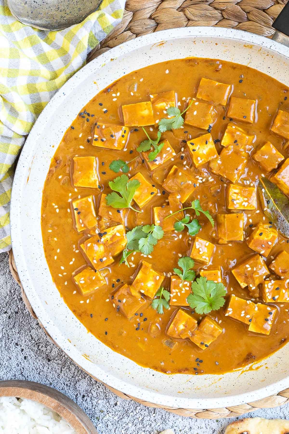 White frying pan with a creamy orange sauce mixed with tofu cubes, sprinkled with sesame seeds and freshly chopped cilantro.