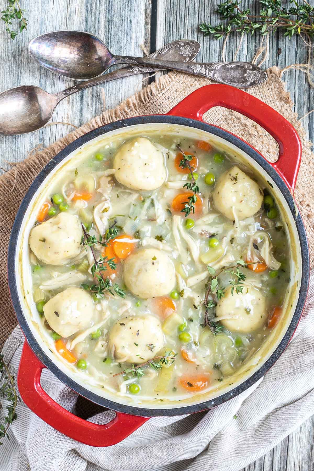 A red-white enameled Dutch oven with dumplings, chopped veggies, shredded mushroom pieces in place of chicken, green herbs in a thick, white stew.