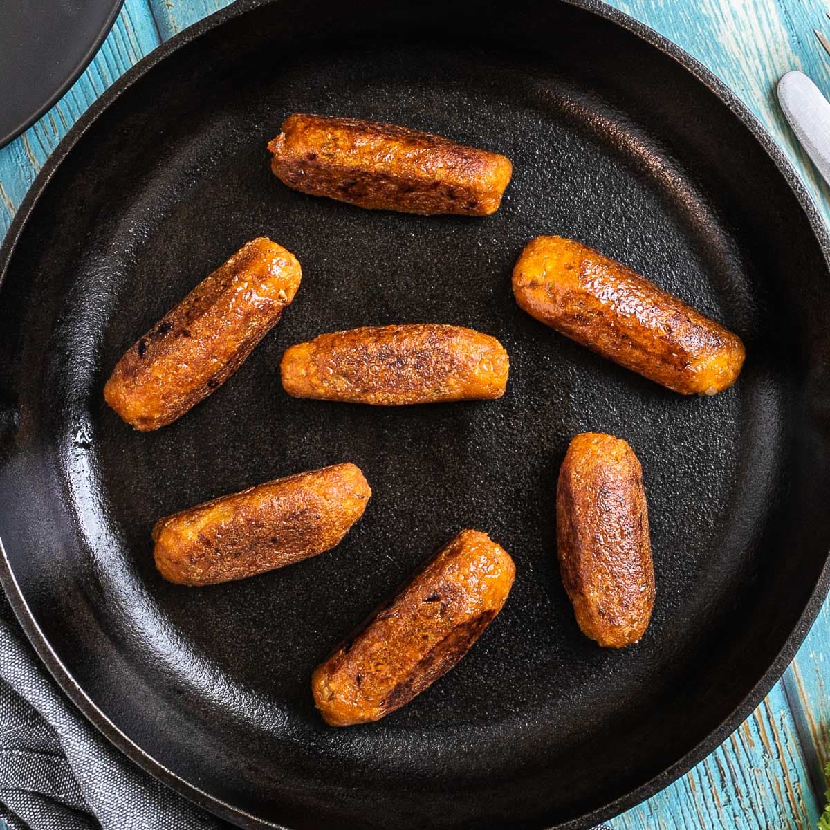 7 small sausages in a black cast-iron skillet.