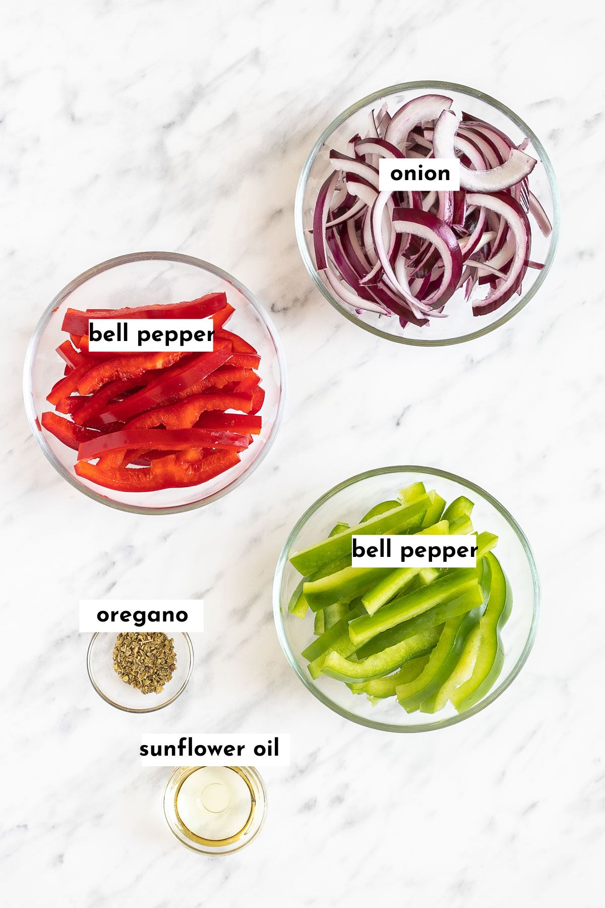 The ingredients of chipotle fajita veggies are placed in small glass bowls like red and green bell pepper strips, red onion slices, dried oregano, and oil. 