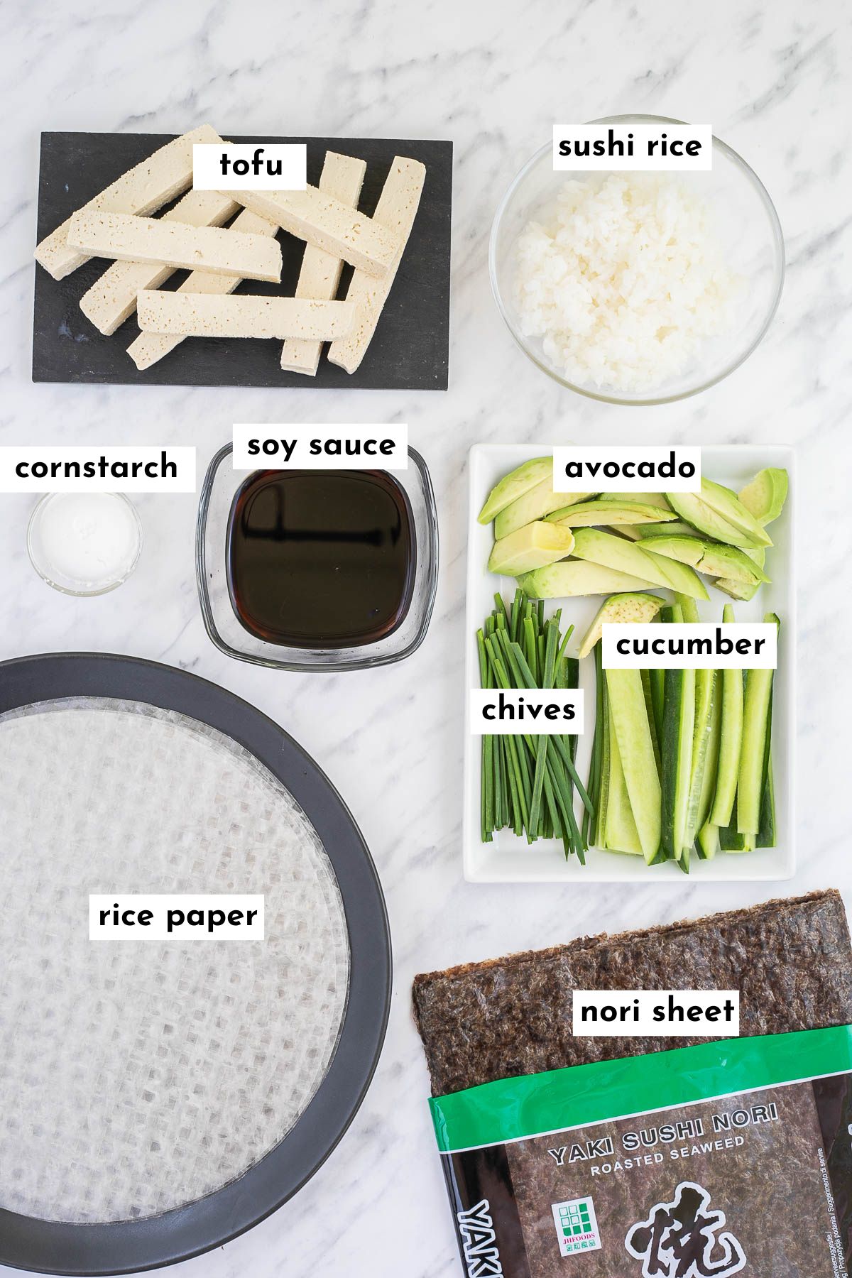 The ingredients of sushi spring rolls are placed in small containers like rice, cucumber sticks, avocado slices, chives, raw white tofu steaks, dark brown sauce, white starch and rice paper wrappers.