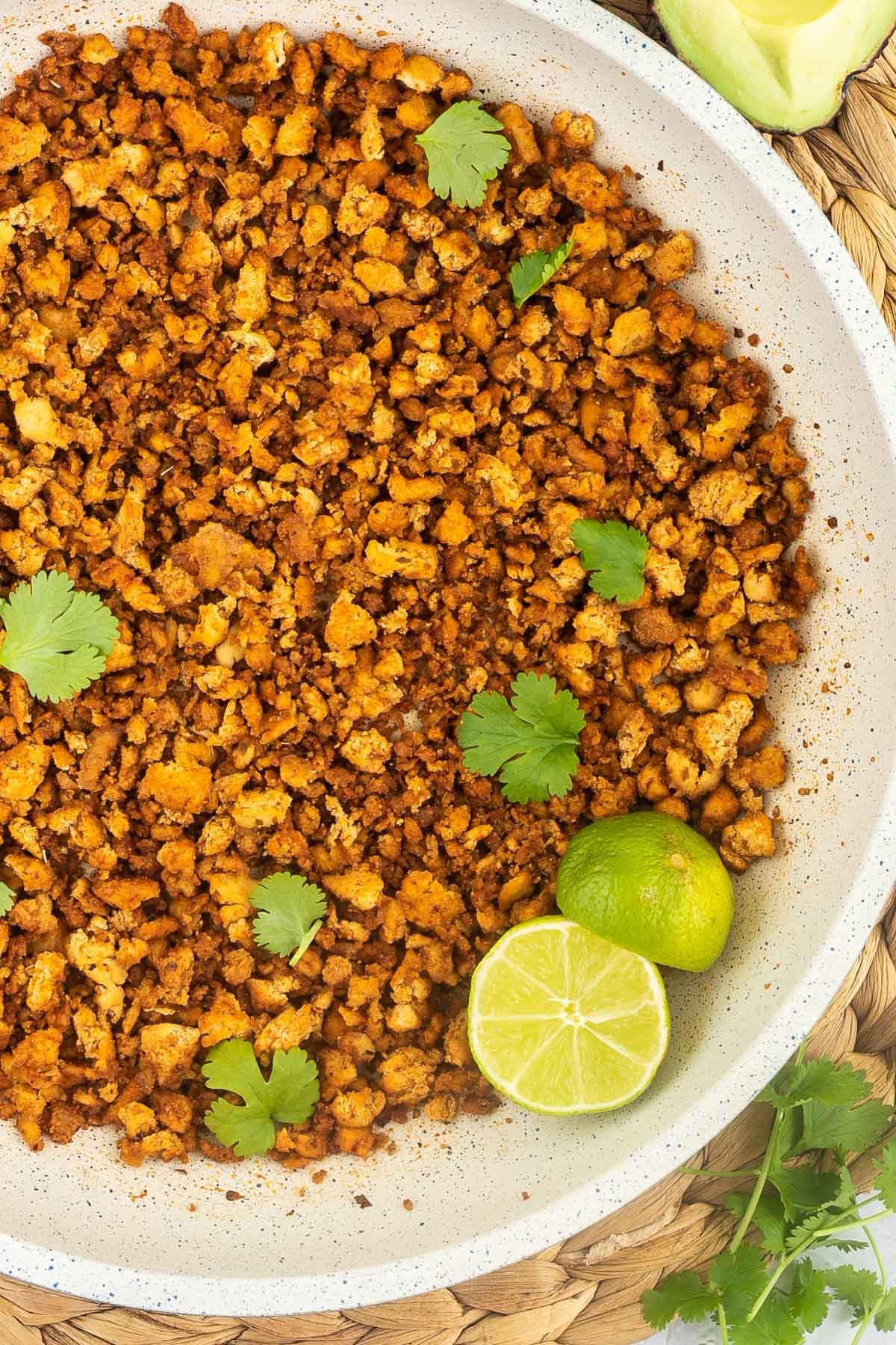 A white frying pan with brown crispy tofu crumbles sprinkled with freshly chopped cilantro. Lime slices are added.
