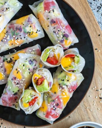 Fresh rice paper wraps filled with chopped tomato, mango, and avocado placed on a black plate. 4 half rolls and 6 whole rolls.