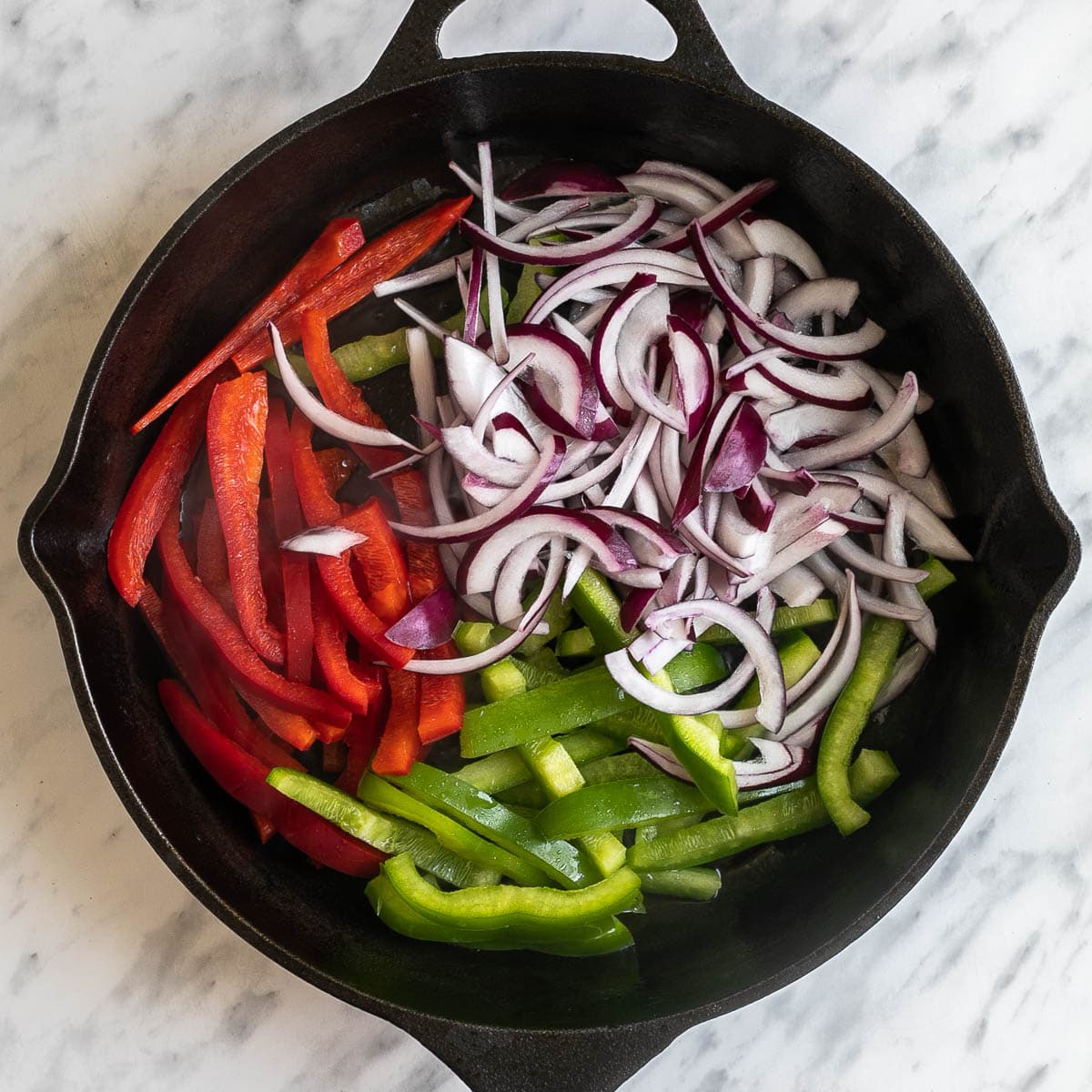 Black cast iron skillet with red and green bell pepper strips and red onion slices.