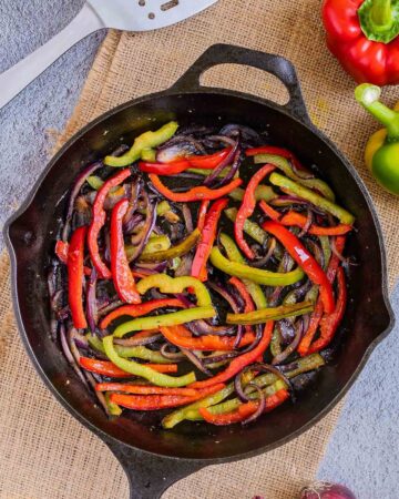 Black cast iron skillet with slightly brown red and green bell pepper strips and red onion slices.