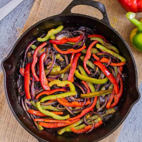 Black cast iron skillet with slightly brown red and green bell pepper strips and red onion slices.