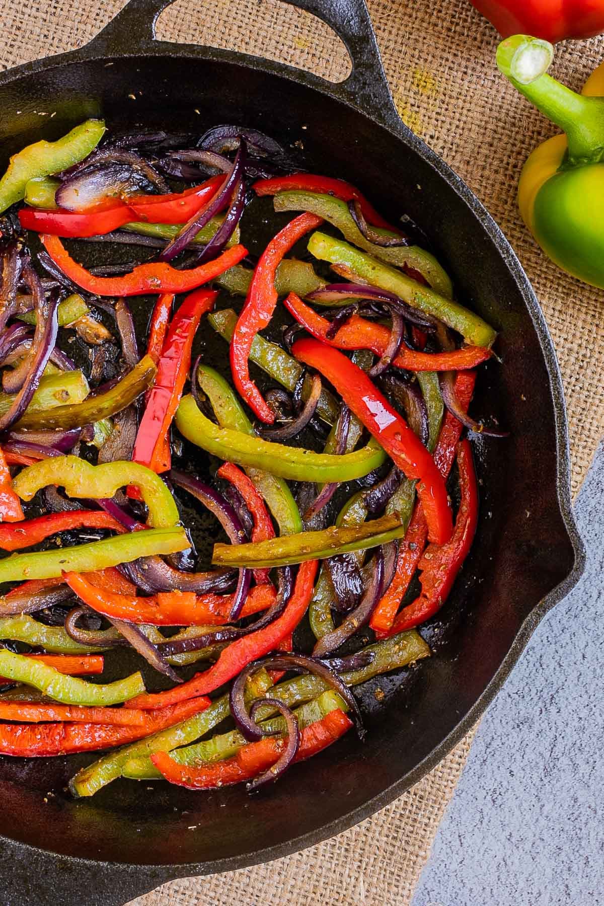 Black cast iron skillet with slightly brown red and green bell pepper strips and red onion slices.