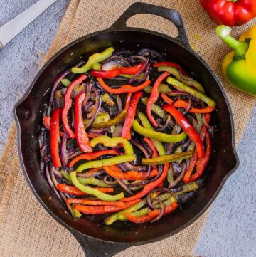 Black cast iron skillet with slightly brown red and green bell pepper strips and red onion slices.