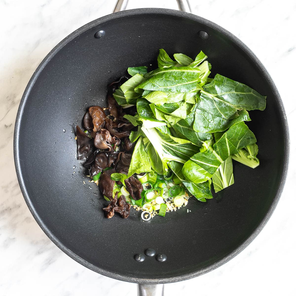 Wok with chopped bok choy, mushroom slices, and chopped onion.