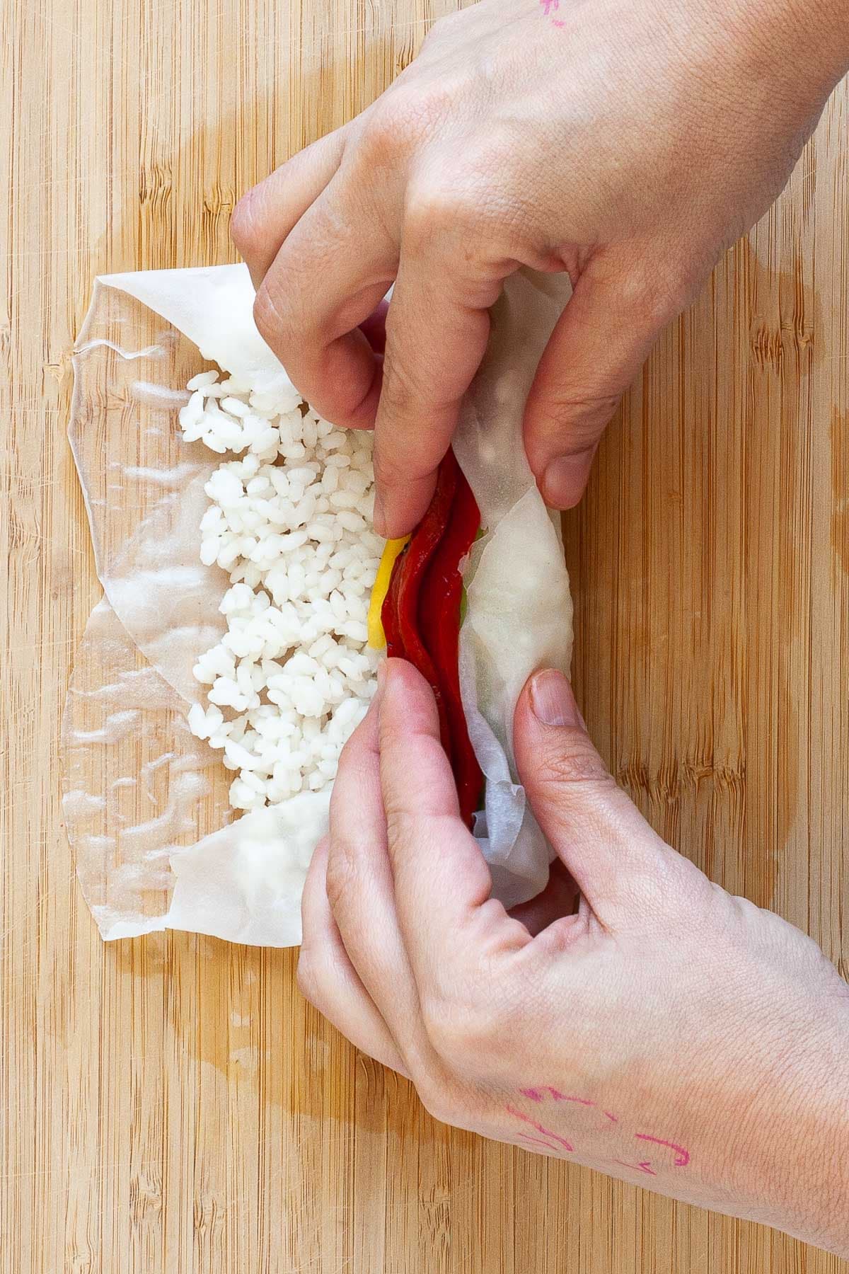 Two hands are folding the soft rice paper wrappers on the filling. 