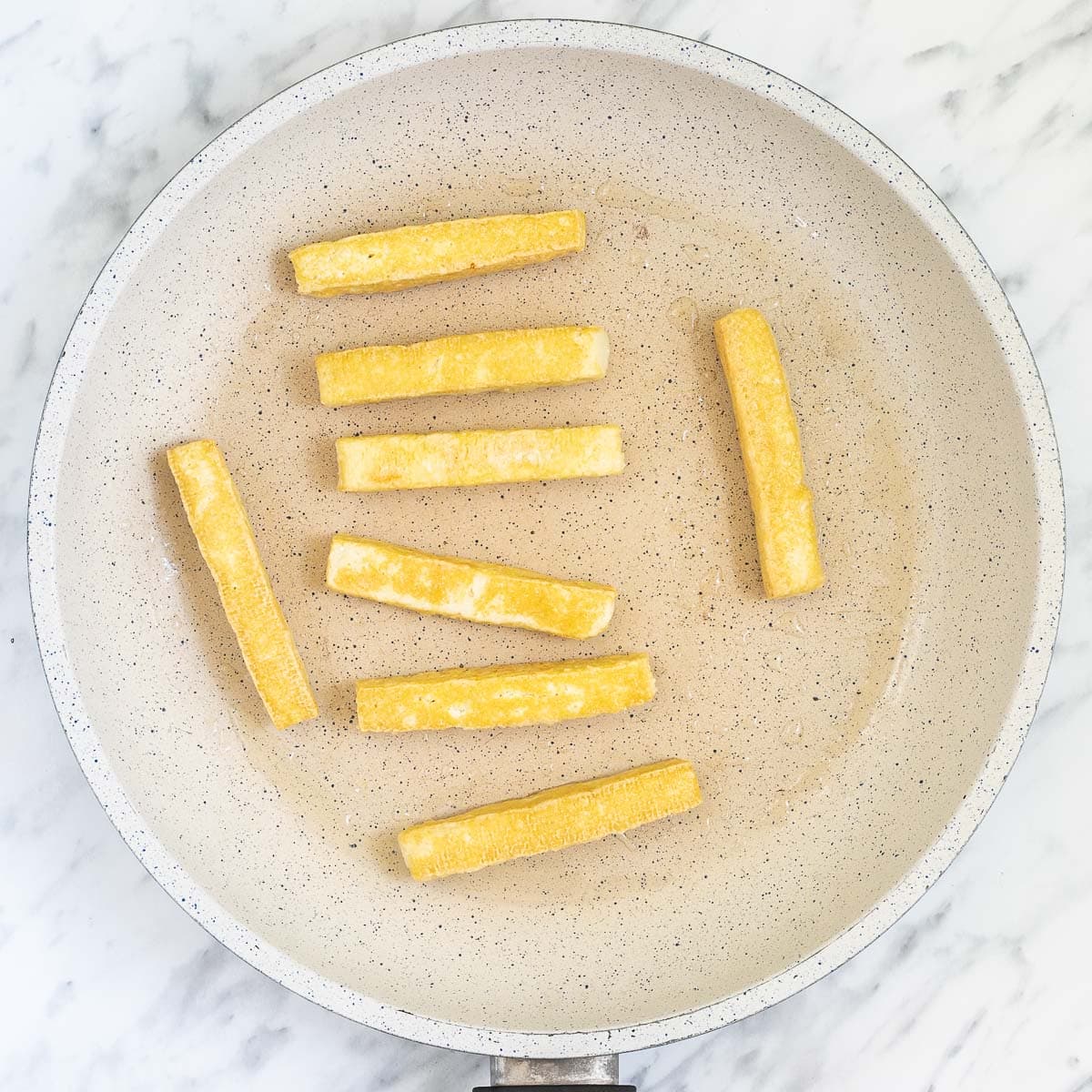 White frying pan with yellow crispy tofu sticks.