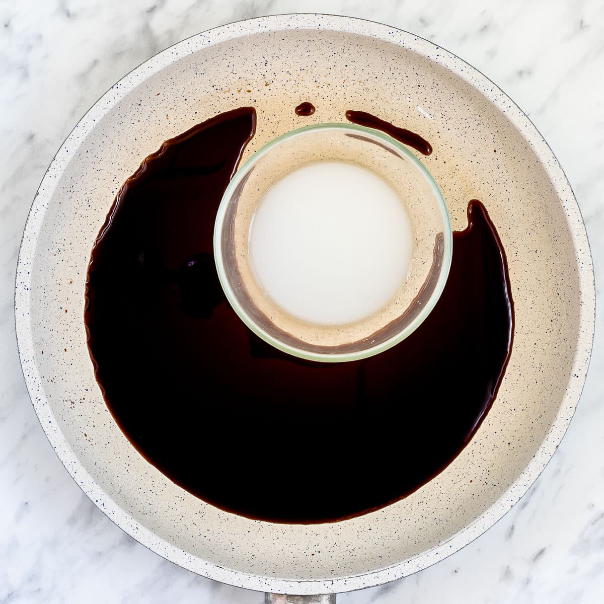 A white frying pan with dark brown liquid. And a small bowl of white liquid.