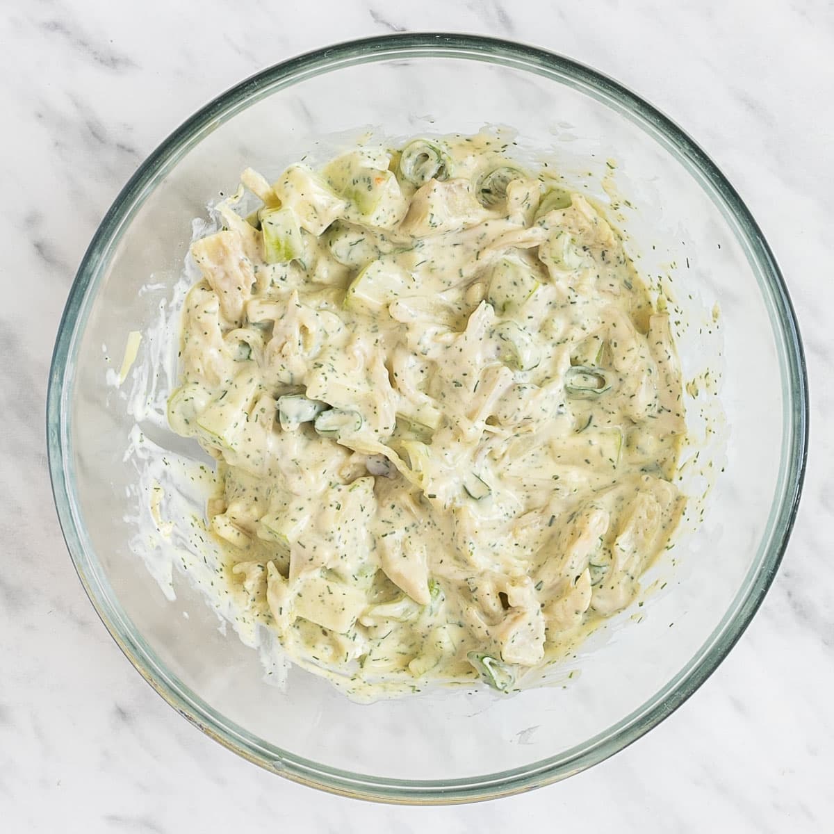 A glass bowl with chopped apples, celery, scallion, and shredded mushrooms covered in a dill white sauce