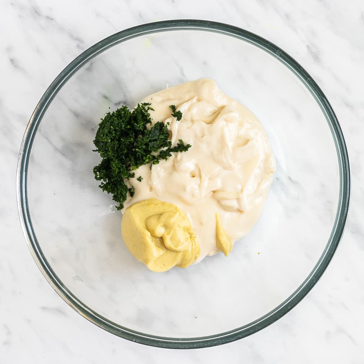 A glass bowl with mayo, mustard and chopped dill.