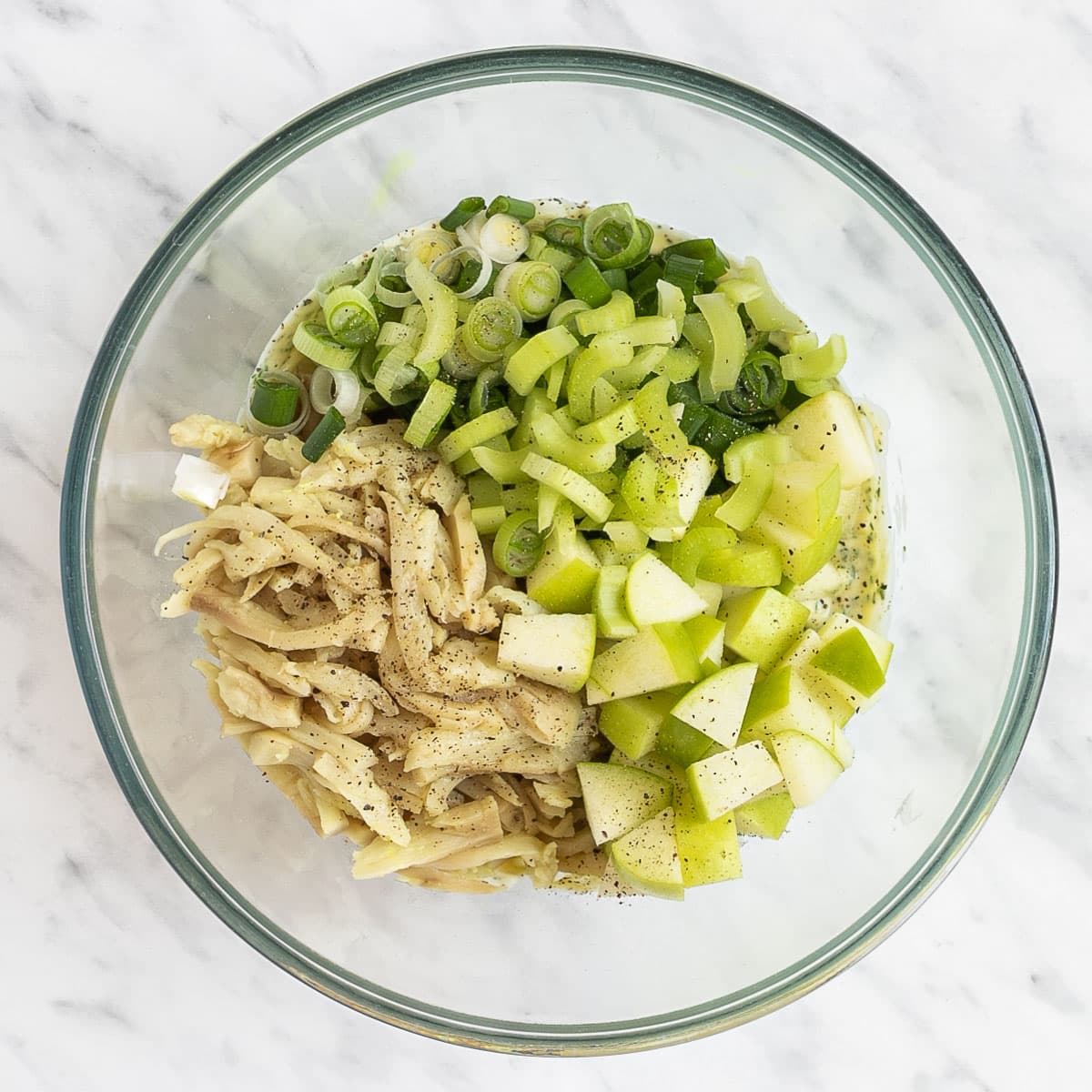 A glass bowl with chopped apples, celery, scallion, and shredded mushrooms