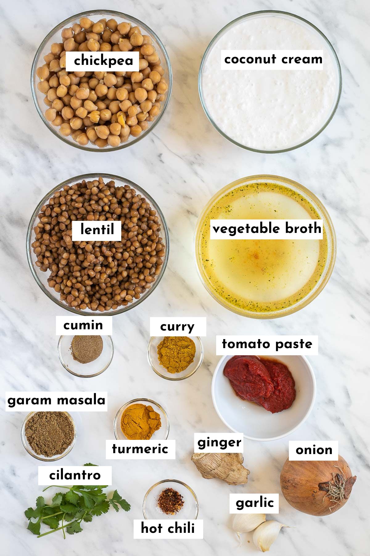 The ingredients of lentil chickpea curry is placed in small glass bowls like chickpeas, lentils, coconut cream, veggie broth, tomato paste, onion, ginger, cilantro, and various spices in different shades of brown, red and yellow. 