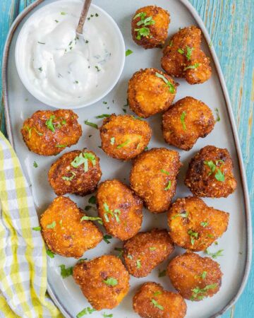 Breaded cauliflower florets in a light blue plate sprinkled with chopped green herbs and served with a small bowl of white sauce