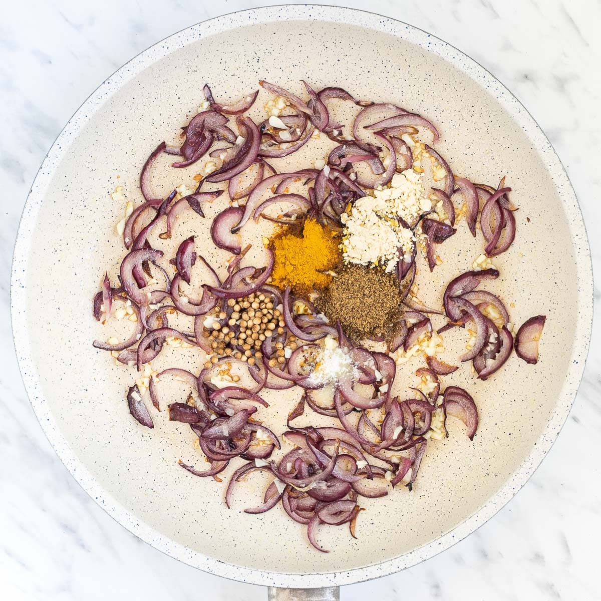 White frying pan with red onion slices and heaps of spices