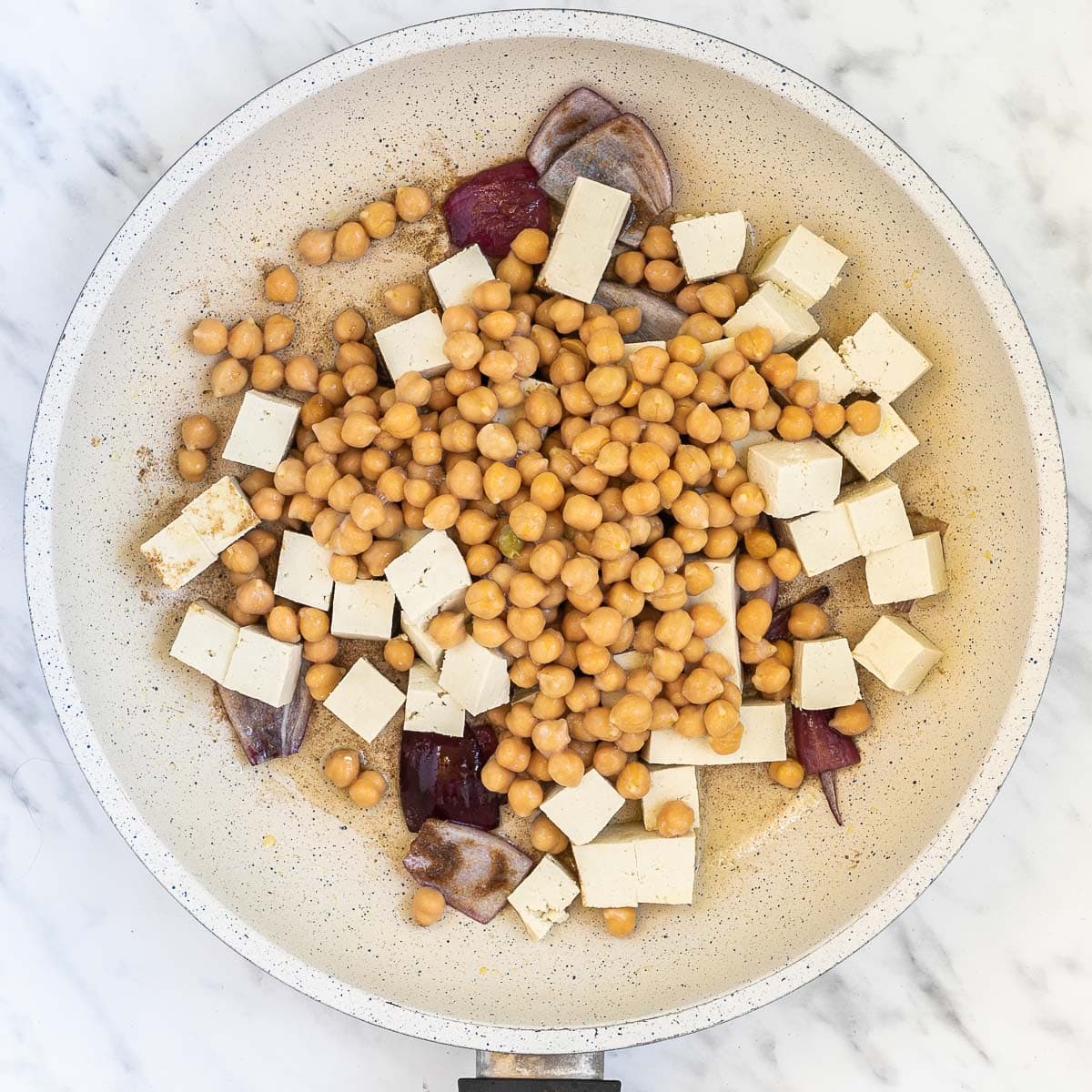 Red onion pieces, tofu cubes, and chickpeas in a white frying pan.