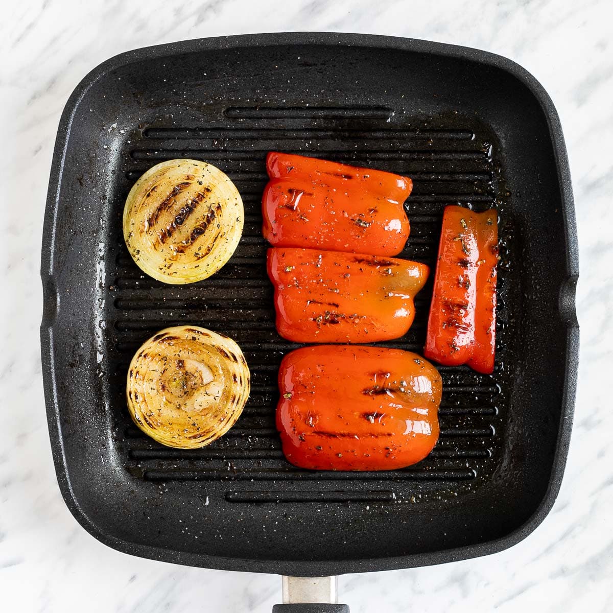 Grill pan with 2 charred onion slices and 4 red bell pepper pieces.