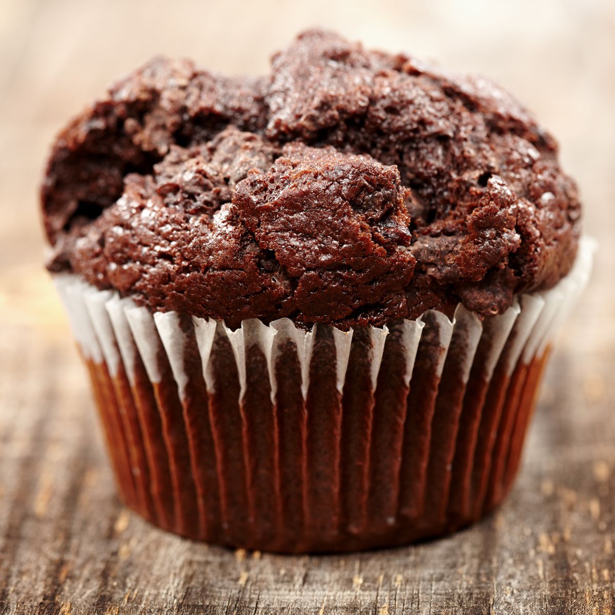 A chocolate muffin up really close on a wooden surface. 