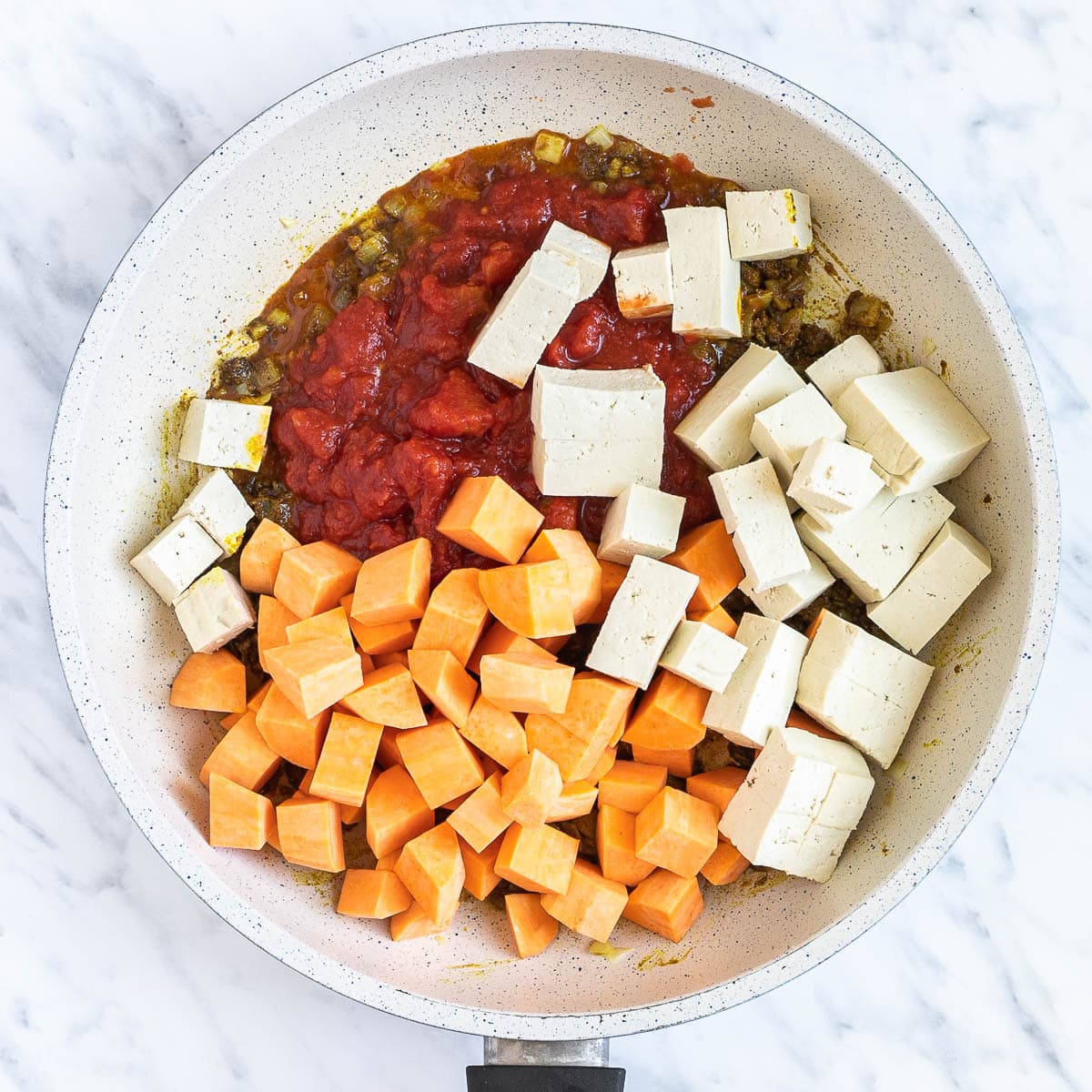 A white frying pan with tomato sauce, chopped orange sweet potato and white tofu cubes.