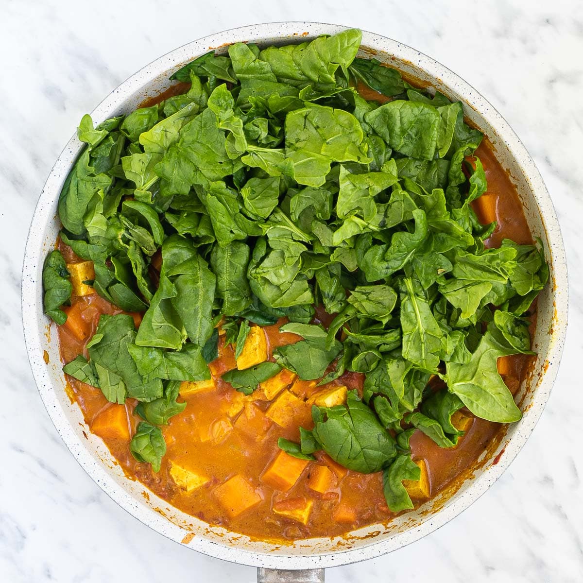 Chopped orange sweet potatoes and tofu cubes in an orange thick sauce. Fresh chopped spinach leaves are on top.