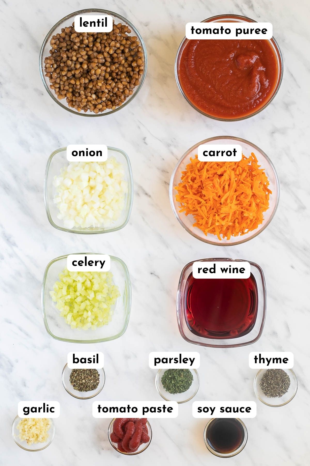 The ingredients of lentil bolognese in small glass bowls like brown lentils, tomato sauce, chopped onions, carrot, celery, red wine and several small bowls of spices.