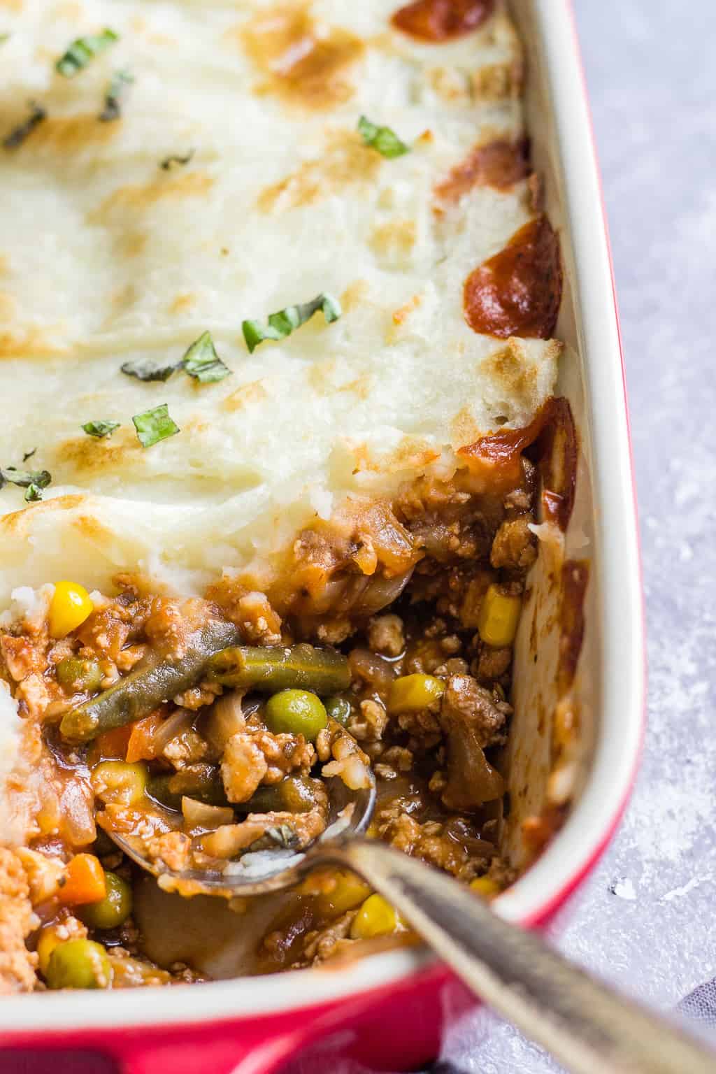 Red and white casserole dish with a veggie and tofu crumble stew topped with mashed potatoes