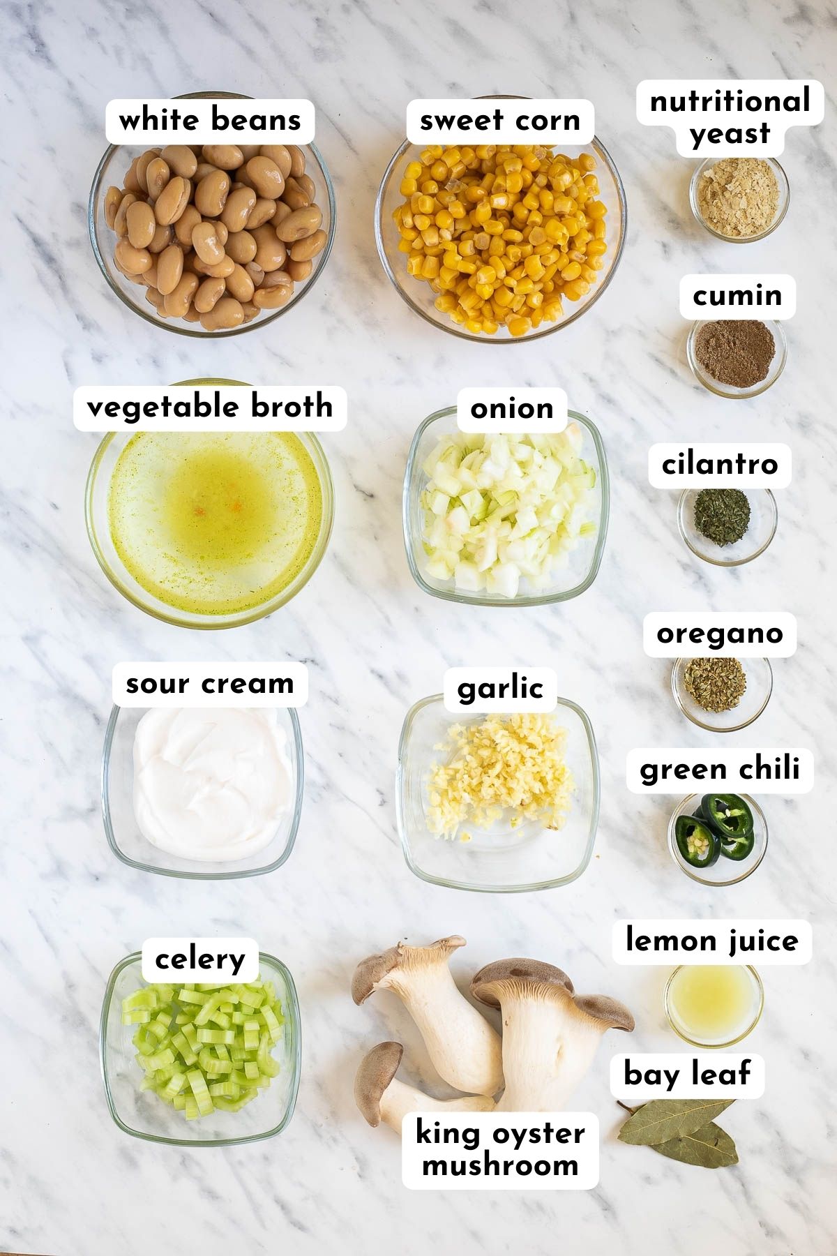Ingredients of vegan white chili are placed into small glass bowls like white beans, king oyster mushrooms, veggie broth, sour cream, celery, garlic, onion, and various spices. 