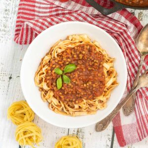 A white bowl of tagliatelle pasta topped with lentils in bolognese sauce.