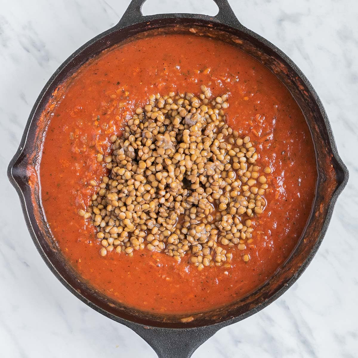 Red chunky sauce with lentils on top in a cast iron skillet