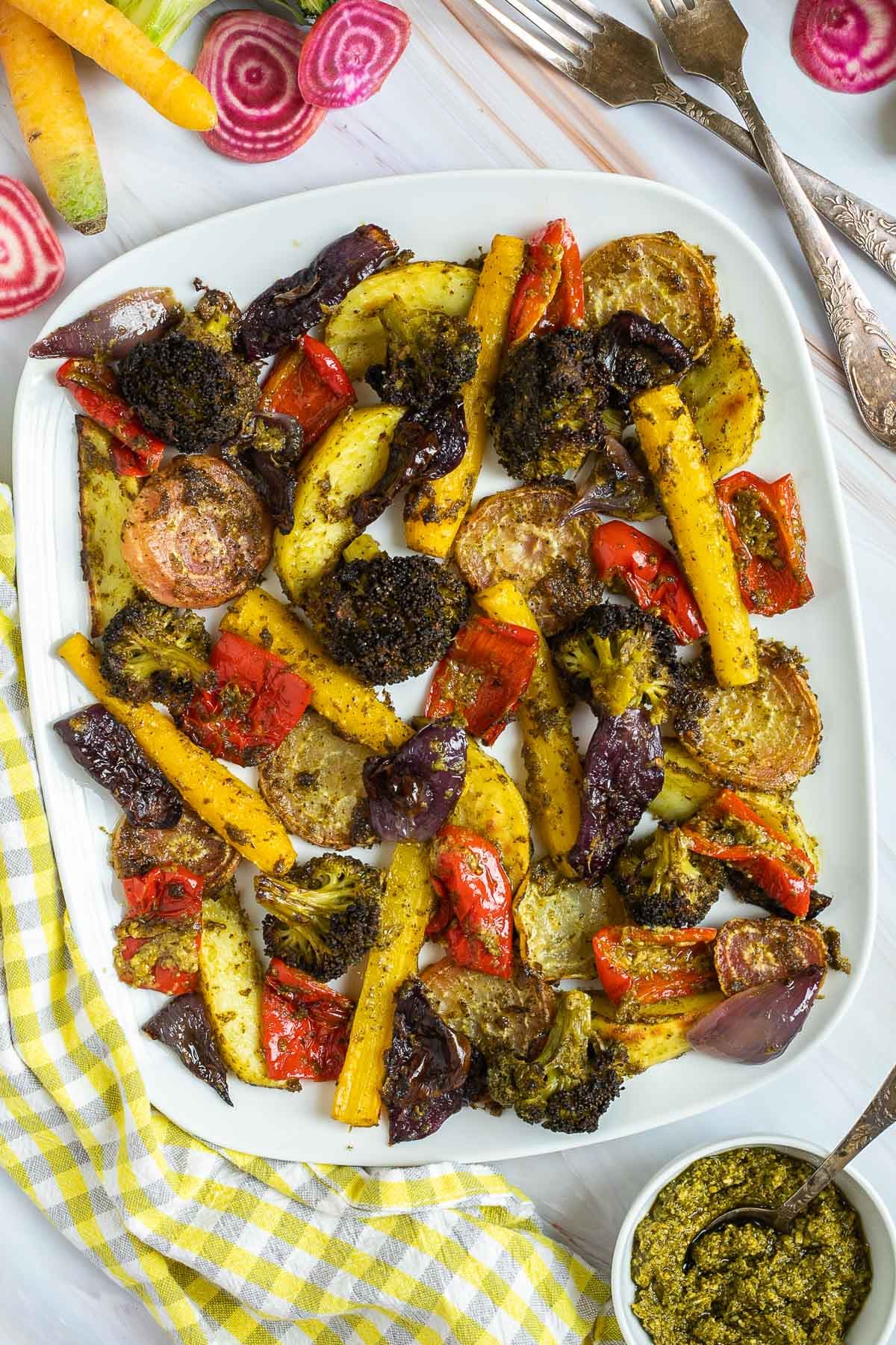 Large white serving plate with vibrant vegetables like broccoli, yellow carrots, red pepper, red onion, pink beet and potato slightly charred around the edges covered in a bit of pesto sauce. 