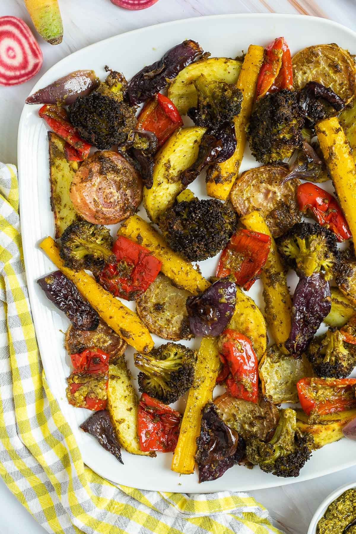 Large white serving plate with vibrant vegetables like broccoli, yellow carrots, red pepper, red onion, pink beet and potato slightly charred around the edges covered in a bit of pesto sauce.